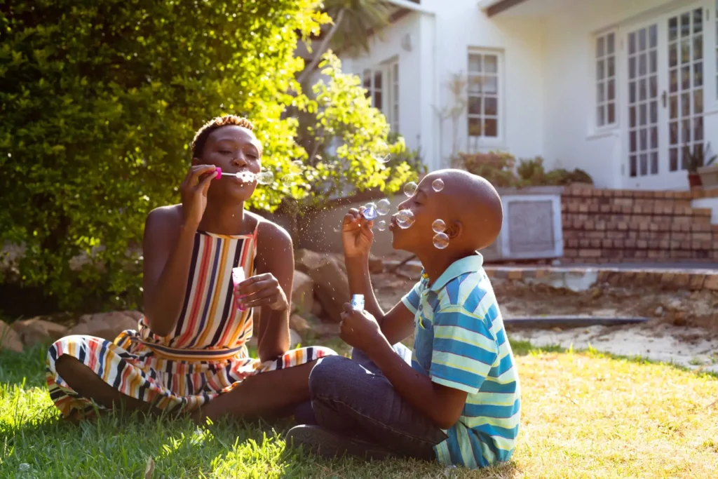 Foster mom blowing bubbles on front yard with her son.